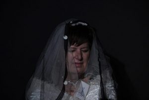 Eine Frau mit Schleier und geschlossenen Augen vor schwarzem Hintergrund.