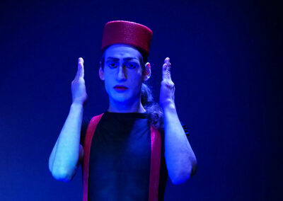 Pascal Scurk in der Rolle des Efi, Proben: Kammerspiel "JETZT!" Der Schauspieler ist stark verfemdend geschmickt, Er trägt eine breiten roten Ring als Hut. Er steht auf schwarzer Bühne.