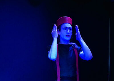 Pascal Scurk in der Rolle des Efi, Proben: Kammerspiel "JETZT!" Der Schauspieler ist stark verfemdend geschmickt, Er trägt eine breiten roten Ring als Hut. Er steht auf schwarzer Bühne.